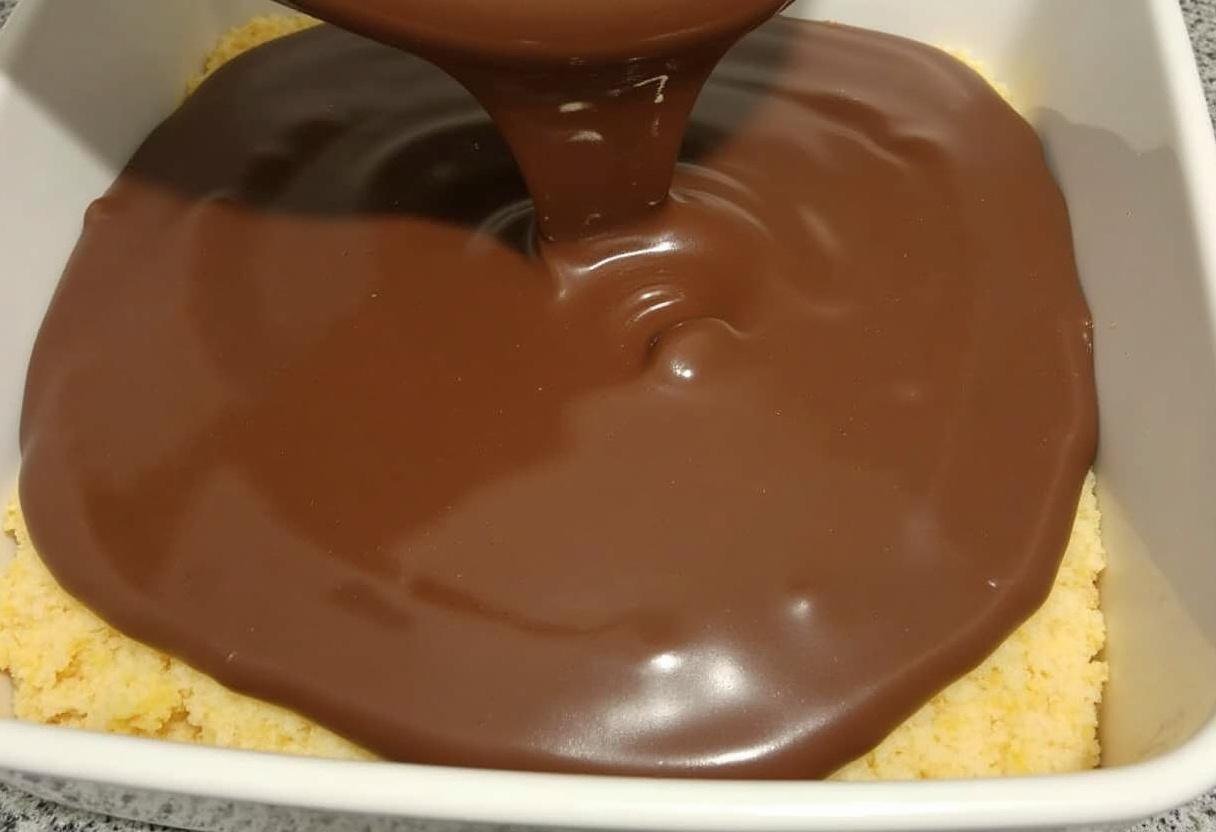 Schokoladenmischung wird über die Keks-Schicht für den Bounty-Kuchen ohne Backen gegossen.