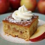 Fertiger Apfelkuchen mit Marzipan, präsentiert auf einem Teller mit Sahne und frischen Äpfeln.