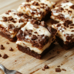 Ein Stück Himmlische Tiramisu Brownies liegt auf einer hellen Walnuss-Holzoberfläche. Darunter eine dunkle, fudgy Brownie-Basis, oben eine cremige Mascarpone-Tiramisu-Schicht, leicht staubt Kakao darüber. Nahaufnahme, warme natürliche Beleuchtung, sanfte Schärfentiefe.