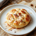 Nahaufnahme eines Milchmädchen-Kuchens: Schichten aus Löffelbiskuits, cremige Dulce de Leche-Füllung, luftige Sahne, sanft mit Kakao bestäubt, serviert auf einem hellen Holzbrett im natürlichen Licht.
