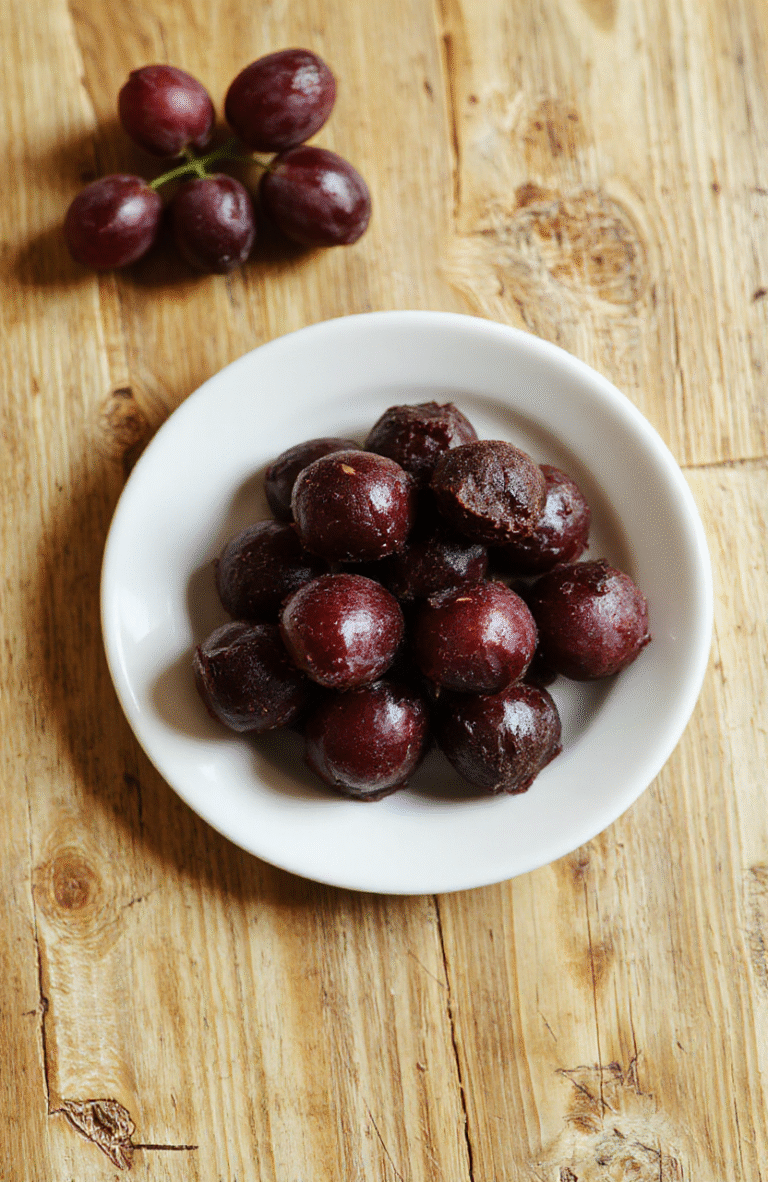 Nahaufnahme von grünen Weintraubenhälften mit dunkler Schokoladenüberzug, garniert mit gehackten Mandeln, auf Backpapier servierfertig.