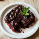 Nahaufnahme eines Stücks Himbeer Brownie Cheesecake auf heller Holzplatte; cremige Cheesecake-Schicht, dunkler Keksboden, rote Himbeeren als Garnitur, glatte Glasur und frische Früchte verleihen Glanz.